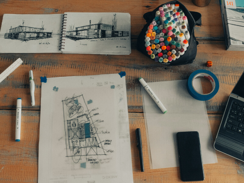 Photos d'un cabinet d'architecture avec un ordinateur, quelques plans de construction et des crayons à dessin